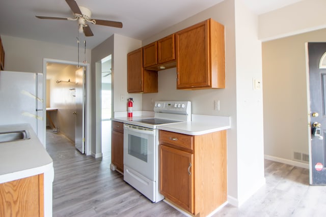 kitchen featuring white appliances, light wood finished floors, brown cabinetry, a ceiling fan, and light countertops