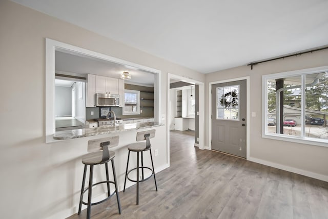 kitchen featuring stainless steel microwave, white cabinetry, a sink, wood finished floors, and a kitchen breakfast bar