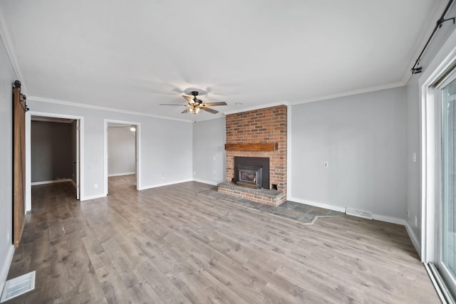 unfurnished living room featuring a ceiling fan, a barn door, visible vents, and wood finished floors