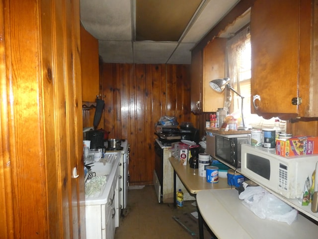 kitchen featuring wooden walls, brown cabinetry, white microwave, stainless steel microwave, and a paneled ceiling