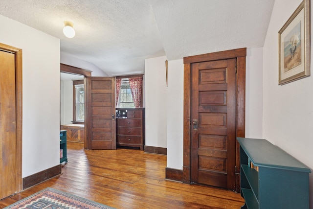 entryway featuring wood-type flooring, baseboards, vaulted ceiling, and a textured ceiling