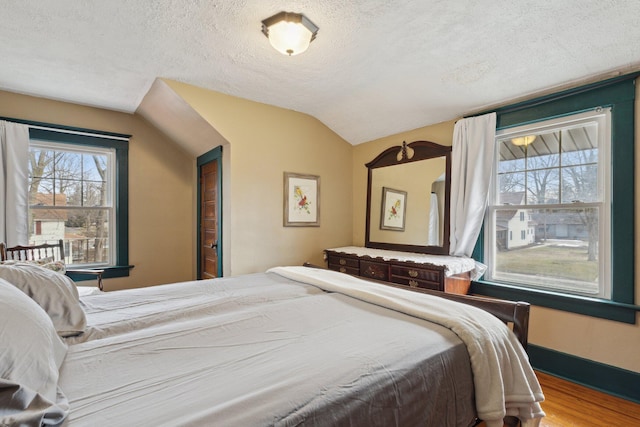 bedroom with vaulted ceiling, a textured ceiling, baseboards, and wood finished floors