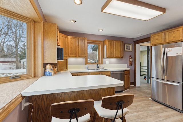 kitchen with light wood-style flooring, appliances with stainless steel finishes, a peninsula, light countertops, and a sink