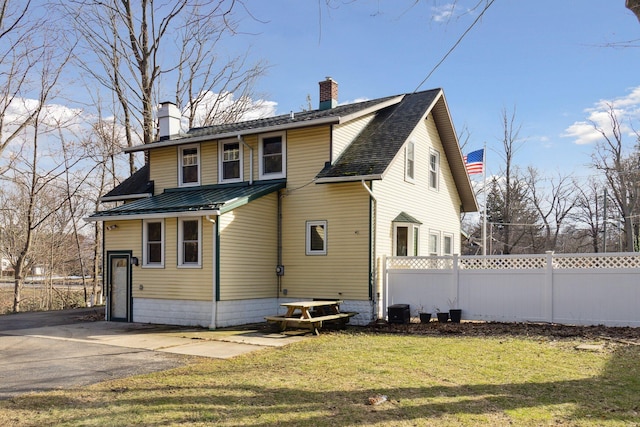 rear view of property featuring central air condition unit, a chimney, fence, and a lawn