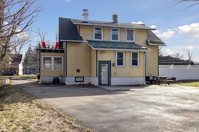 view of front of property with a chimney, a shingled roof, metal roof, fence, and a balcony