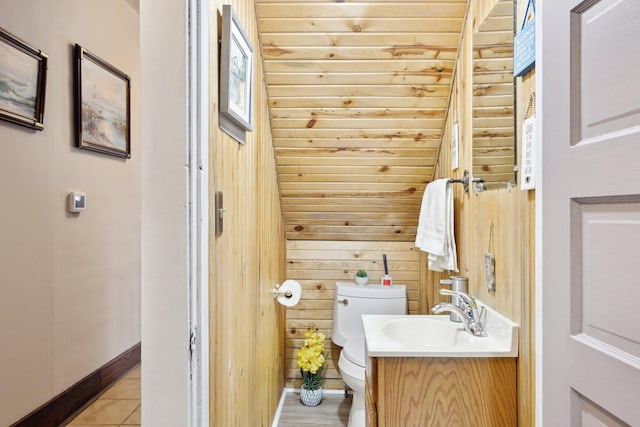 half bathroom with toilet, wood walls, vanity, tile patterned flooring, and baseboards