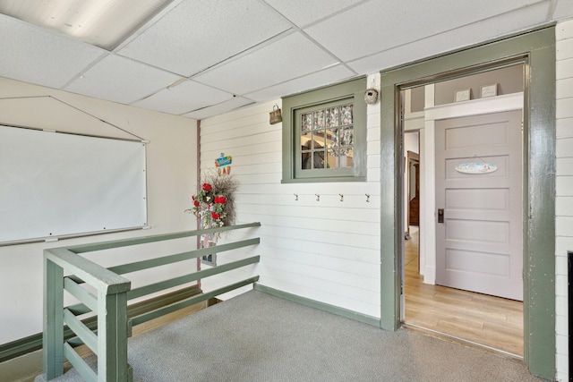 interior space with a drop ceiling and wooden walls