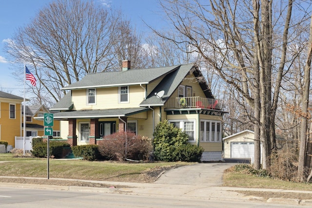 view of front facade with an outbuilding, a balcony, a detached garage, a chimney, and a front yard