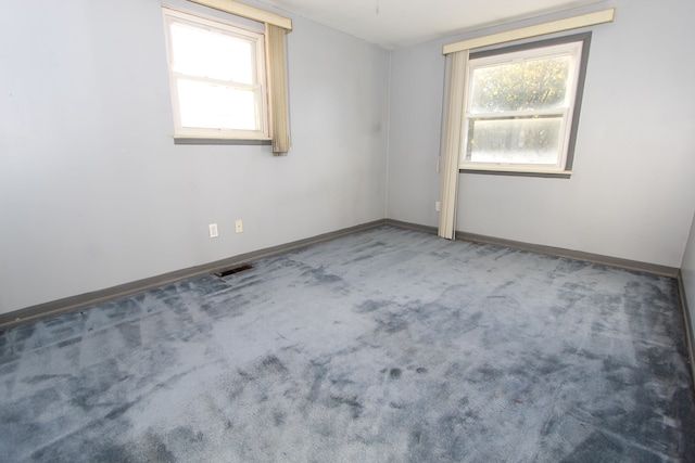 carpeted empty room featuring a wealth of natural light, visible vents, and baseboards