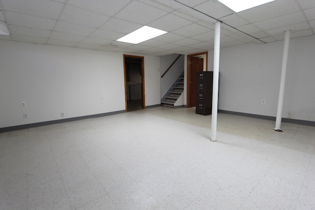 finished basement featuring stairs, baseboards, a paneled ceiling, and tile patterned floors