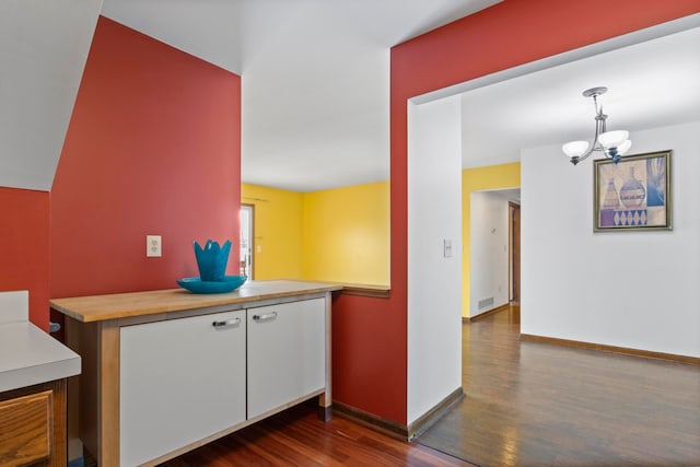 kitchen with dark wood finished floors, visible vents, hanging light fixtures, an inviting chandelier, and baseboards