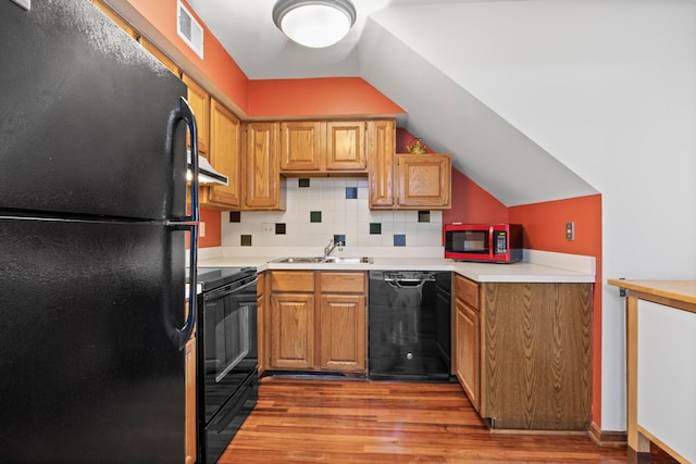 kitchen featuring visible vents, lofted ceiling, light wood-type flooring, black appliances, and a sink