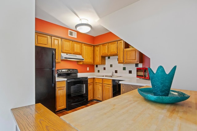 kitchen with visible vents, backsplash, a sink, under cabinet range hood, and black appliances