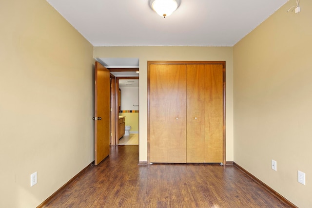 unfurnished bedroom featuring a closet, dark wood finished floors, and baseboards