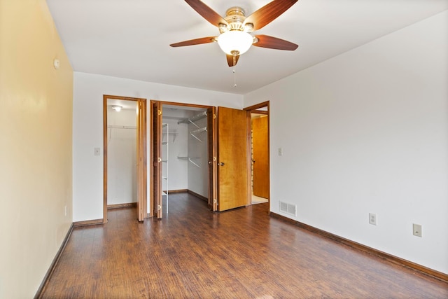 unfurnished bedroom with baseboards, visible vents, dark wood finished floors, a walk in closet, and a closet