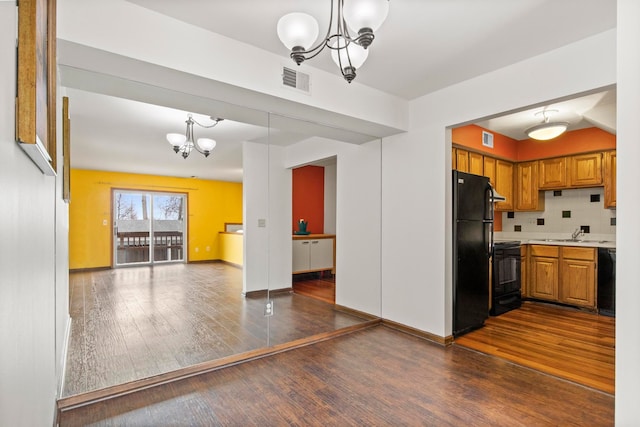 kitchen featuring brown cabinets, black appliances, a chandelier, and open floor plan