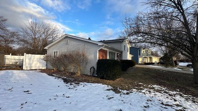 view of snowy exterior featuring fence and brick siding