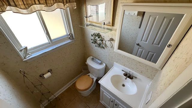 half bath featuring wallpapered walls, baseboards, toilet, tile patterned floors, and vanity