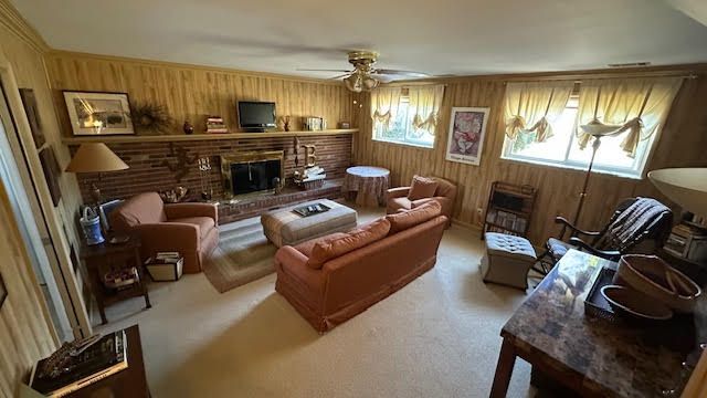 carpeted living room featuring wooden walls, a fireplace, and ceiling fan