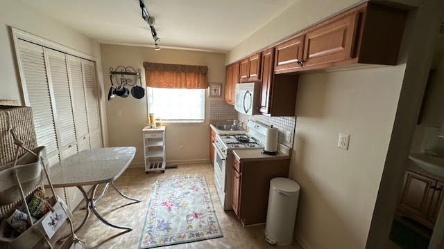 kitchen featuring backsplash, baseboards, white range with gas stovetop, brown cabinets, and rail lighting