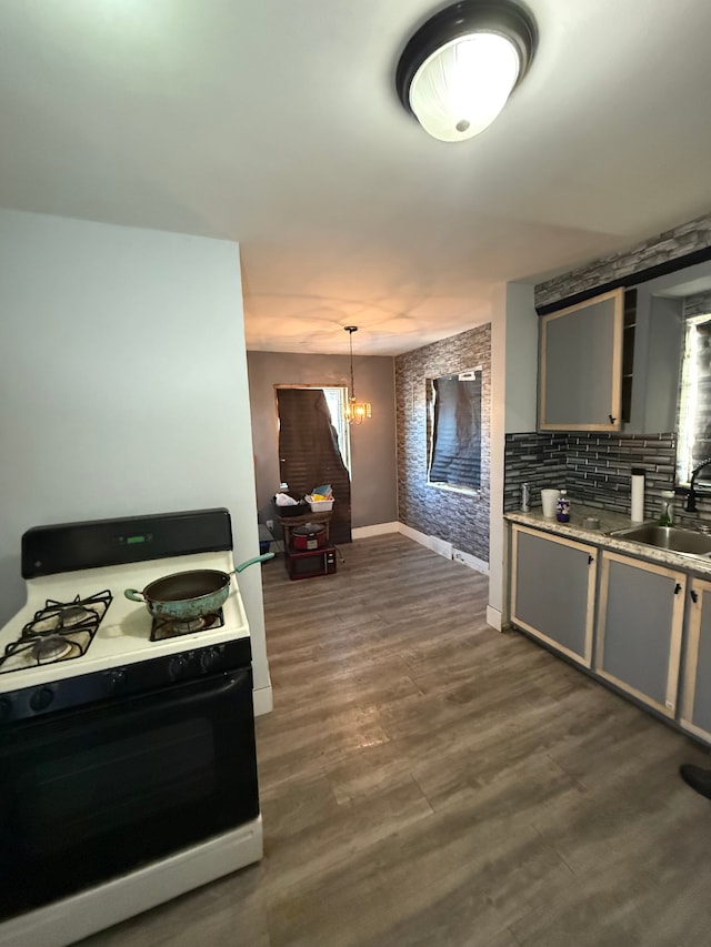 kitchen featuring gas range, dark wood-type flooring, a sink, gray cabinetry, and a notable chandelier