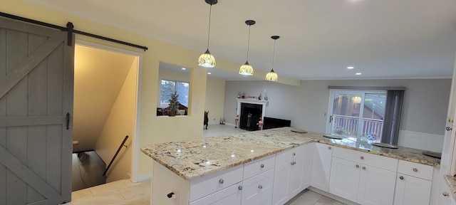 kitchen with a barn door, a fireplace, white cabinetry, and light stone countertops