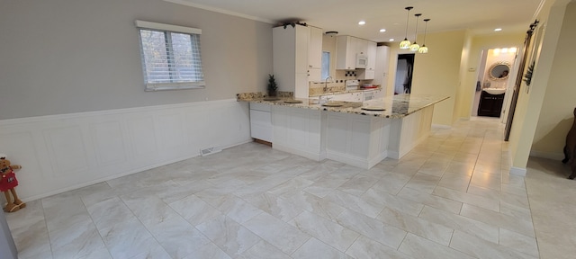 kitchen featuring wainscoting, a peninsula, light stone countertops, white cabinetry, and a sink