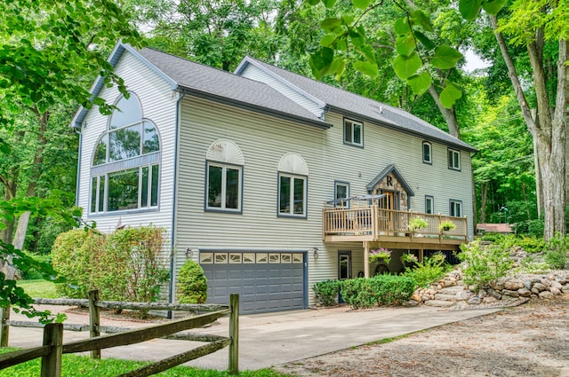 view of front of property with a deck, an attached garage, concrete driveway, and roof with shingles