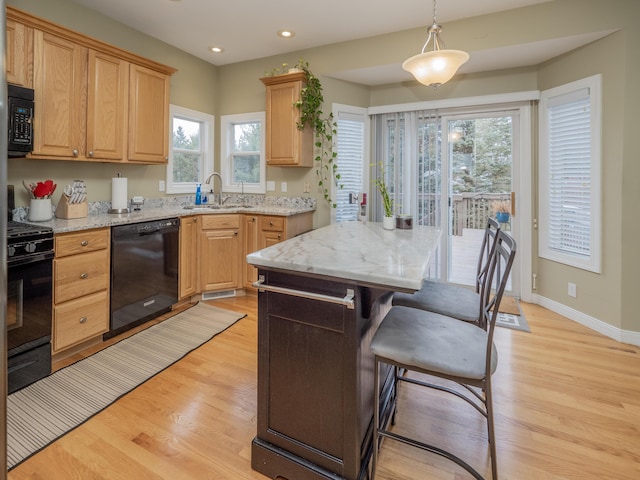 kitchen featuring light wood-style floors, light stone counters, a breakfast bar area, black appliances, and a sink