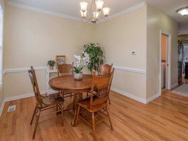 dining space with visible vents, baseboards, ornamental molding, light wood-type flooring, and an inviting chandelier