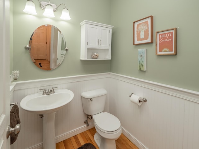 half bathroom with a wainscoted wall, toilet, and wood finished floors