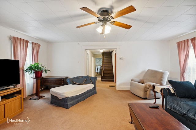 living area featuring light carpet, visible vents, stairway, and a ceiling fan