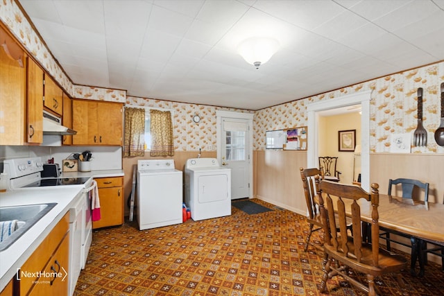 kitchen featuring wallpapered walls, electric range, wainscoting, under cabinet range hood, and washing machine and dryer