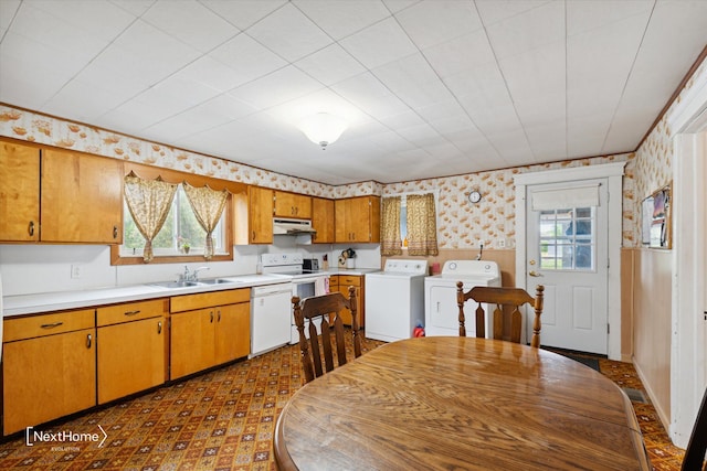 kitchen with wallpapered walls, white appliances, washer and clothes dryer, under cabinet range hood, and a sink