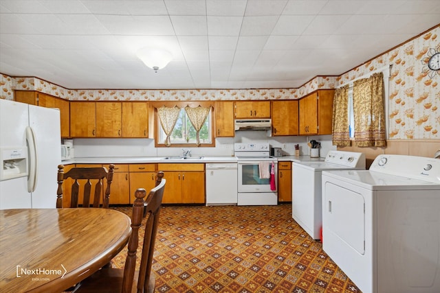 kitchen featuring under cabinet range hood, white appliances, brown cabinetry, washer and clothes dryer, and wallpapered walls