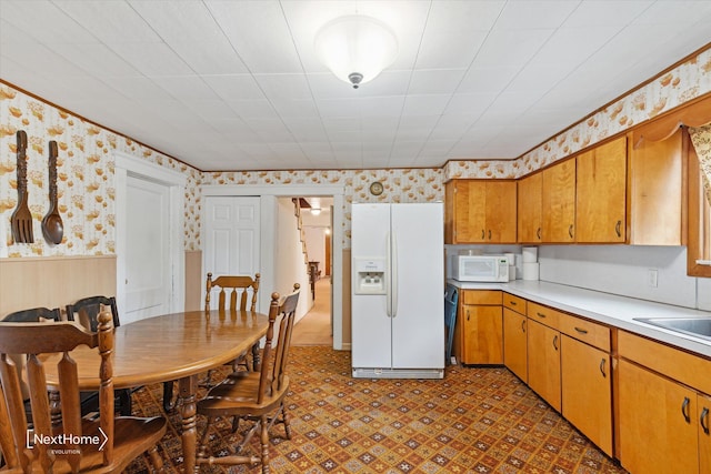 kitchen with wallpapered walls, white appliances, a wainscoted wall, tile patterned floors, and light countertops