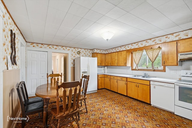 kitchen with under cabinet range hood, white appliances, a sink, light countertops, and wallpapered walls