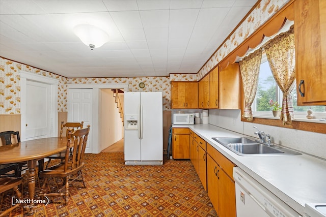 kitchen featuring light countertops, brown cabinetry, a sink, white appliances, and wallpapered walls