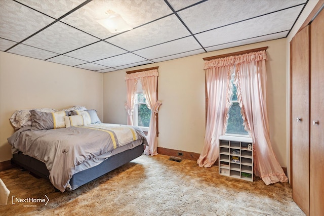 carpeted bedroom with visible vents, a closet, a paneled ceiling, and baseboards