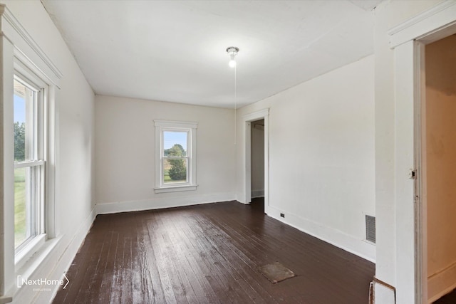 empty room featuring dark wood-style floors, visible vents, and baseboards