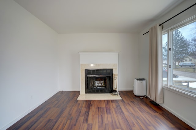 unfurnished living room with a fireplace with raised hearth, wood finished floors, a wealth of natural light, and baseboards