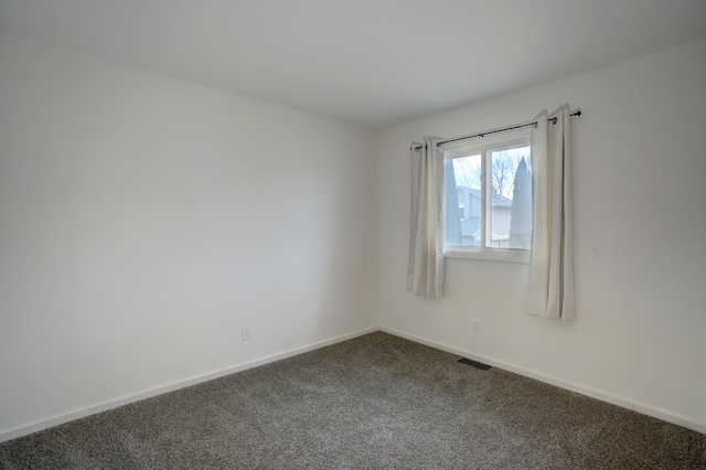 spare room with dark carpet, visible vents, and baseboards