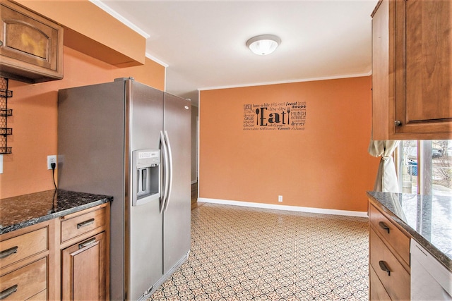 kitchen with brown cabinets, stainless steel refrigerator with ice dispenser, dark stone countertops, dishwasher, and baseboards