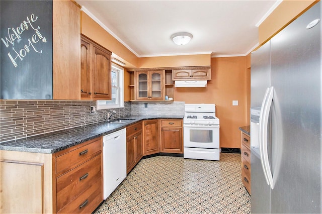 kitchen featuring decorative backsplash, brown cabinetry, a sink, dark stone counters, and white appliances