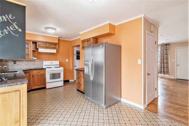 kitchen featuring white gas range oven, stainless steel fridge with ice dispenser, dark countertops, ornamental molding, and under cabinet range hood