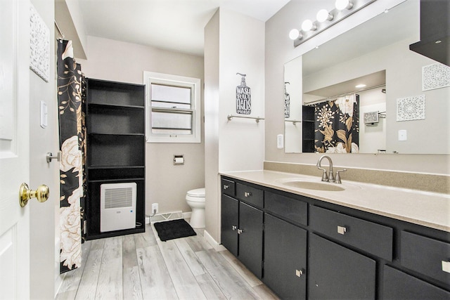 bathroom with toilet, wood finished floors, vanity, baseboards, and heating unit