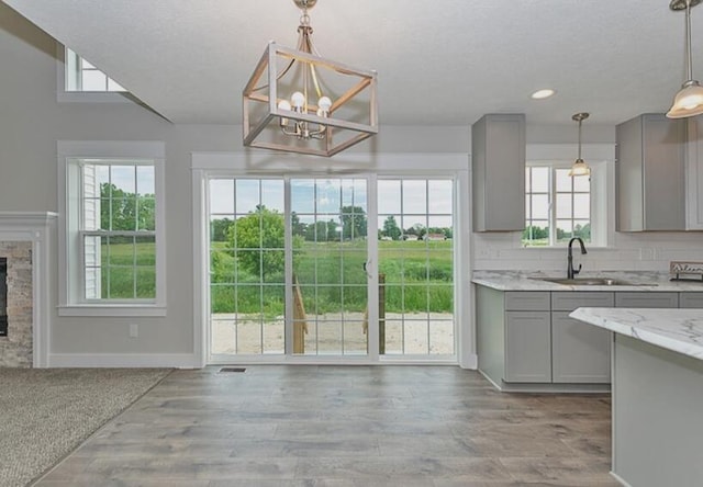 kitchen with a fireplace, decorative backsplash, gray cabinetry, a sink, and light stone countertops