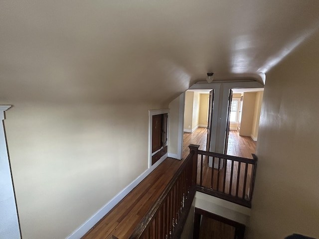 hall featuring an upstairs landing, lofted ceiling, baseboards, and wood finished floors