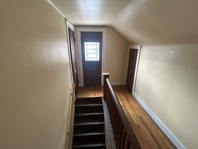 staircase featuring lofted ceiling, baseboards, and wood finished floors