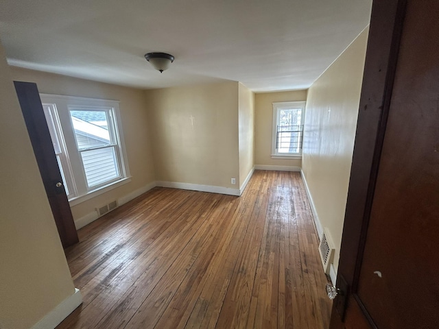 empty room featuring visible vents, hardwood / wood-style flooring, and baseboards